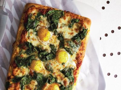 Homemade cheesy spinach pizza with eggs on top