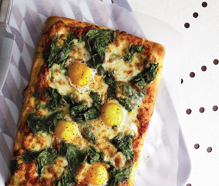Homemade cheesy spinach pizza with eggs on top